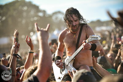 Joel O'Keeffe of Airbourne performing his guitar solo atop a security guard, deep in the crowd at Wacken Open Air 2026.