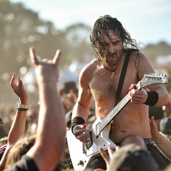 Joel O'Keeffe of Airbourne performing his guitar solo atop a security guard, deep in the crowd at Wacken Open Air 2026.