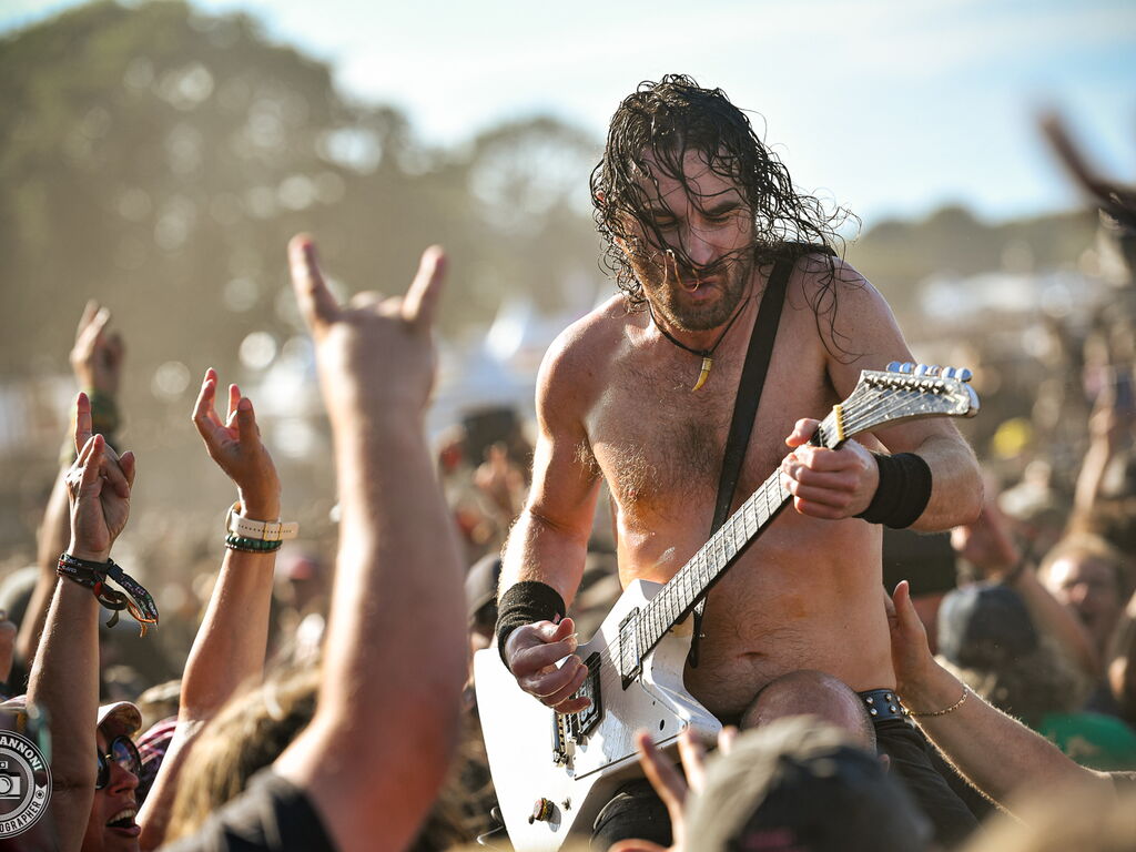 Joel O'Keeffe of Airbourne performing his guitar solo atop a security guard, deep in the crowd at Wacken Open Air 2026.