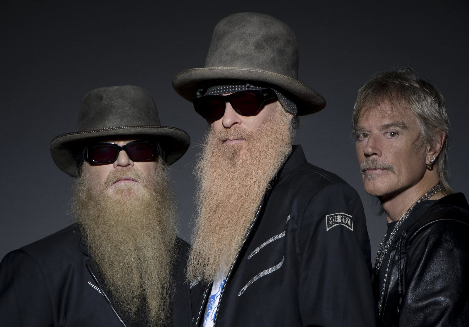 Le trio ZZ Top : Billy Gibbons et Dusty Hill avec leurs barbes emblématiques, aux côtés de Frank Beard, seul membre du groupe sans barbe